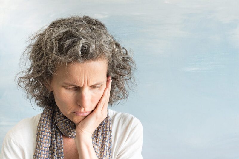 Middle aged woman with wavy grey hair and scarf frowning and looking down while holding face in concern (selective focus)