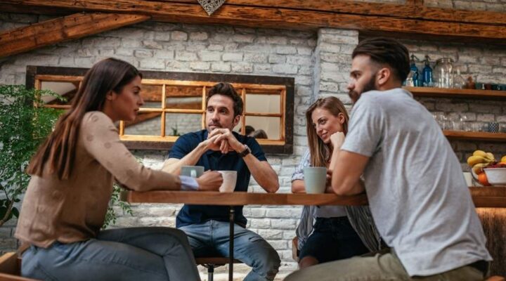 Four friends sit at a table in a cozy café, engaged in a serious conversation over coffee.