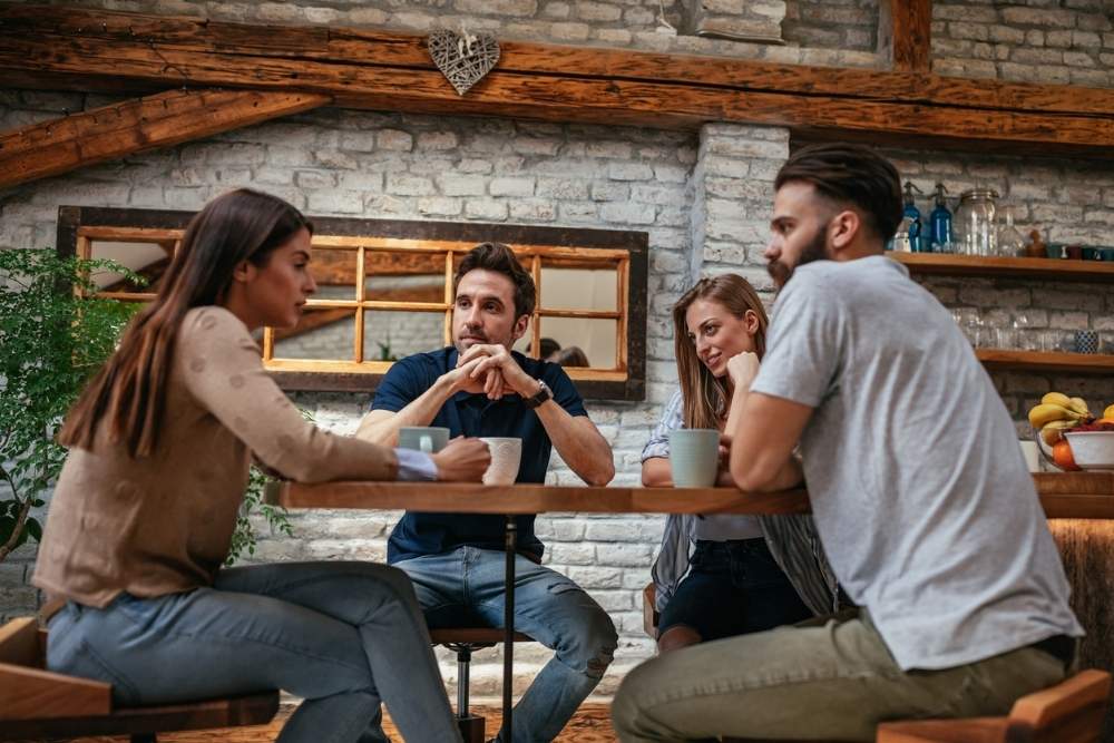 Four friends sit at a table in a cozy café, engaged in a serious conversation over coffee.