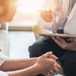 Doctor holding a clipboard and speaking with a patient during a medical consultation, discussing treatment or detox options.