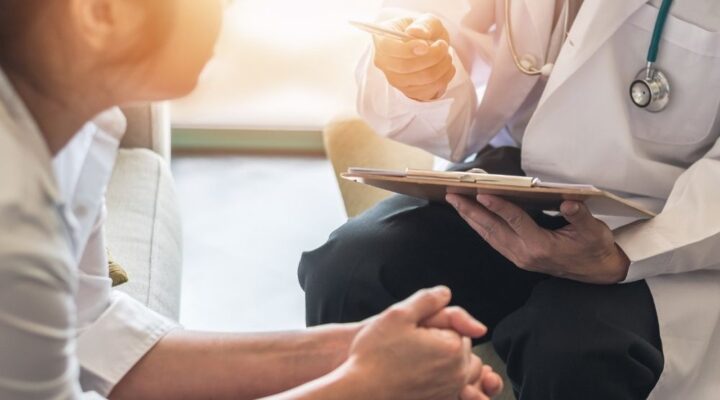 Doctor holding a clipboard and speaking with a patient during a medical consultation, discussing treatment or detox options.