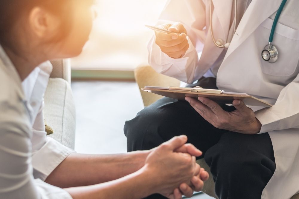 Doctor holding a clipboard and speaking with a patient during a medical consultation, discussing treatment or detox options.