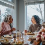 Family gathered around a dining table enjoying a meal together, with two women smiling and talking in a bright, cozy room.