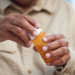 A person opens a prescription pill bottle, symbolizing opioid use, medication management, or preparation for detox and recovery.