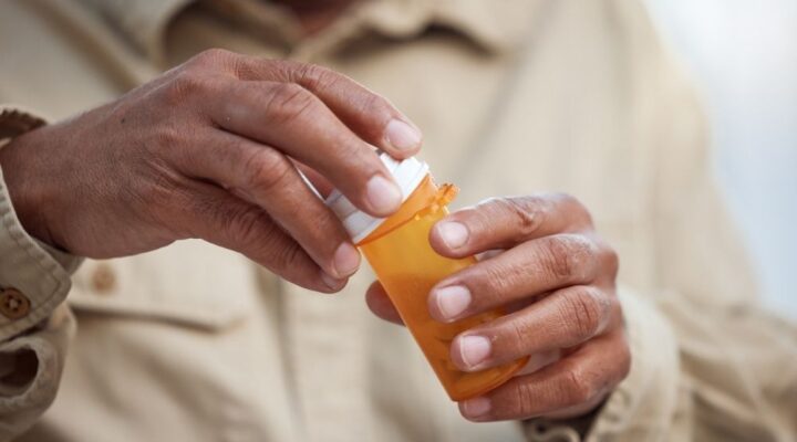 A person opens a prescription pill bottle, symbolizing opioid use, medication management, or preparation for detox and recovery.