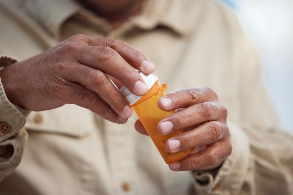 A person opens a prescription pill bottle, symbolizing opioid use, medication management, or preparation for detox and recovery.