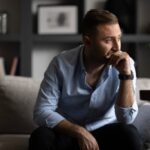 A man sitting on a couch with a sad expression, conveying feelings of loneliness or distress.