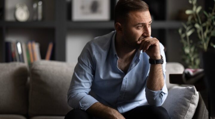 A man sitting on a couch with a sad expression, conveying feelings of loneliness or distress.