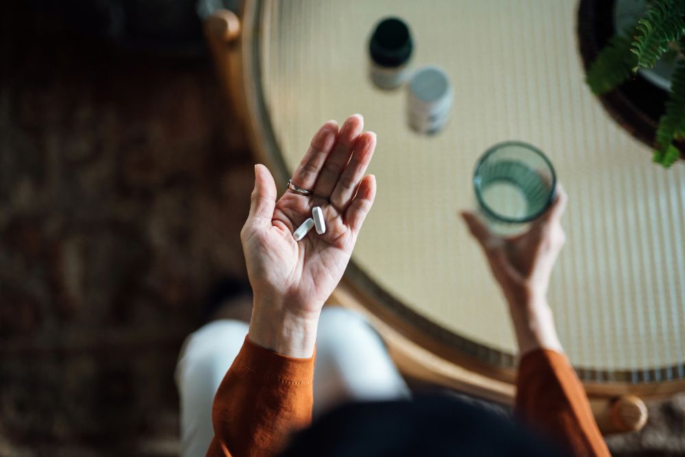 Person holding prescription pills in one hand and a glass of water in the other, viewed from above, representing medication use or treatment.