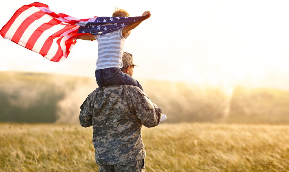 photo of military veteran with child on shoulders holding a flag